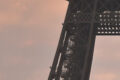 Tour Eiffel vue en contre-plongée au coucher du soleil, ciel aux teintes orangées et roses