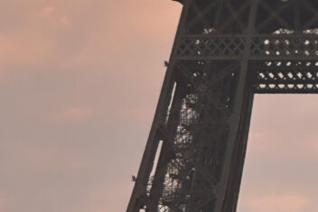 Tour Eiffel vue en contre-plongée au coucher du soleil, ciel aux teintes orangées et roses
