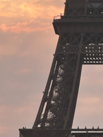 Tour Eiffel vue en contre-plongée au coucher du soleil, ciel aux teintes orangées et roses