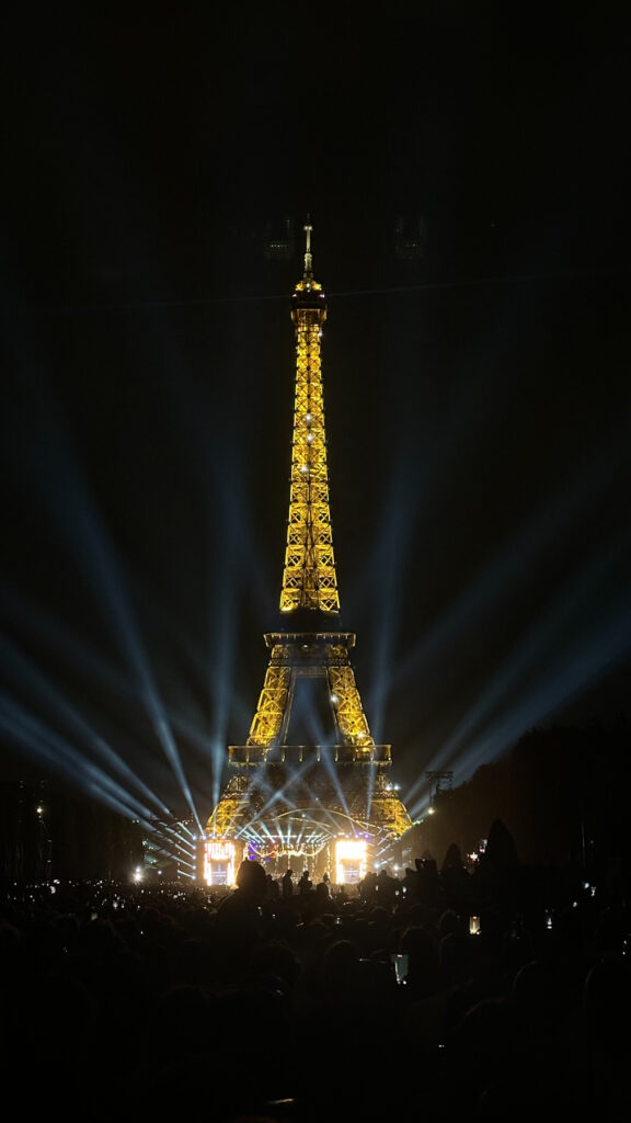 La tour Eiffel illuminée de nuit avec des faisceaux lumineux et une foule rassemblée au pied du monument
