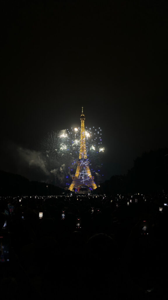 La tour Eiffel illuminée la nuit avec un feu d'artifice éclatant, entourée d'une foule de spectateurs au Champ-de-Mars