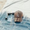 Casquette New York Yankees beige, lunettes de soleil, montre et smartphone posés sur une serviette de plage bleue