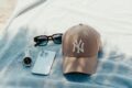 Casquette New York Yankees beige, lunettes de soleil, montre et smartphone posés sur une serviette de plage bleue
