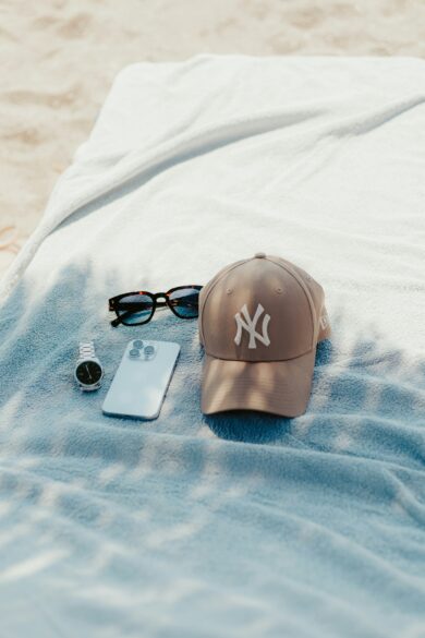 Casquette New York Yankees beige, lunettes de soleil, montre et smartphone posés sur une serviette de plage bleue