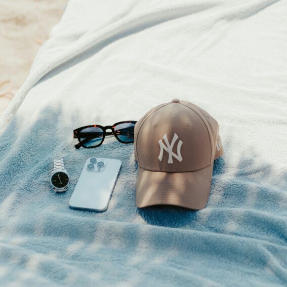 Casquette New York Yankees beige, lunettes de soleil, montre et smartphone posés sur une serviette de plage bleue