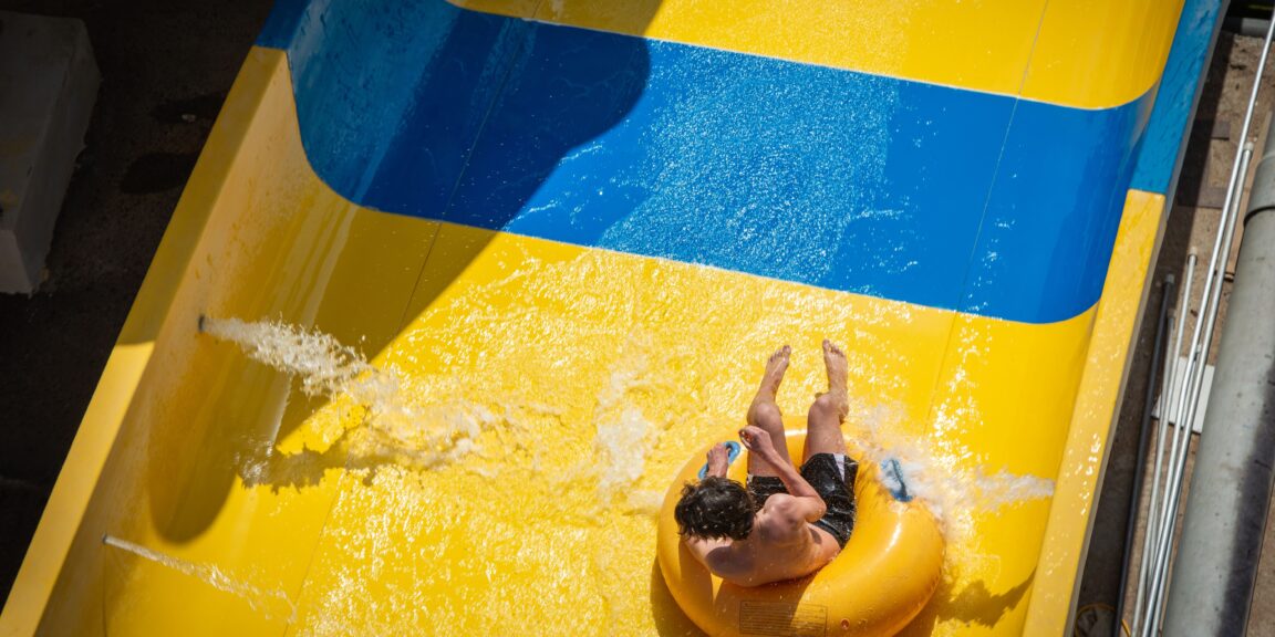 Vue aérienne d'une personne dévalant un toboggan aquatique jaune et bleu sur une bouée