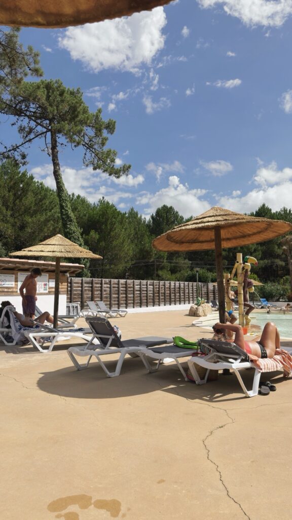 Transats sous parasols en paille près d'une piscine, avec des vacanciers se détendant au soleil au camping Eurosol