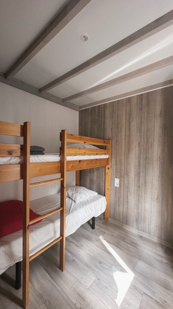 Chambre avec deux lits superposés en bois, literie blanche, mur en lambris et sol effet parquet clair